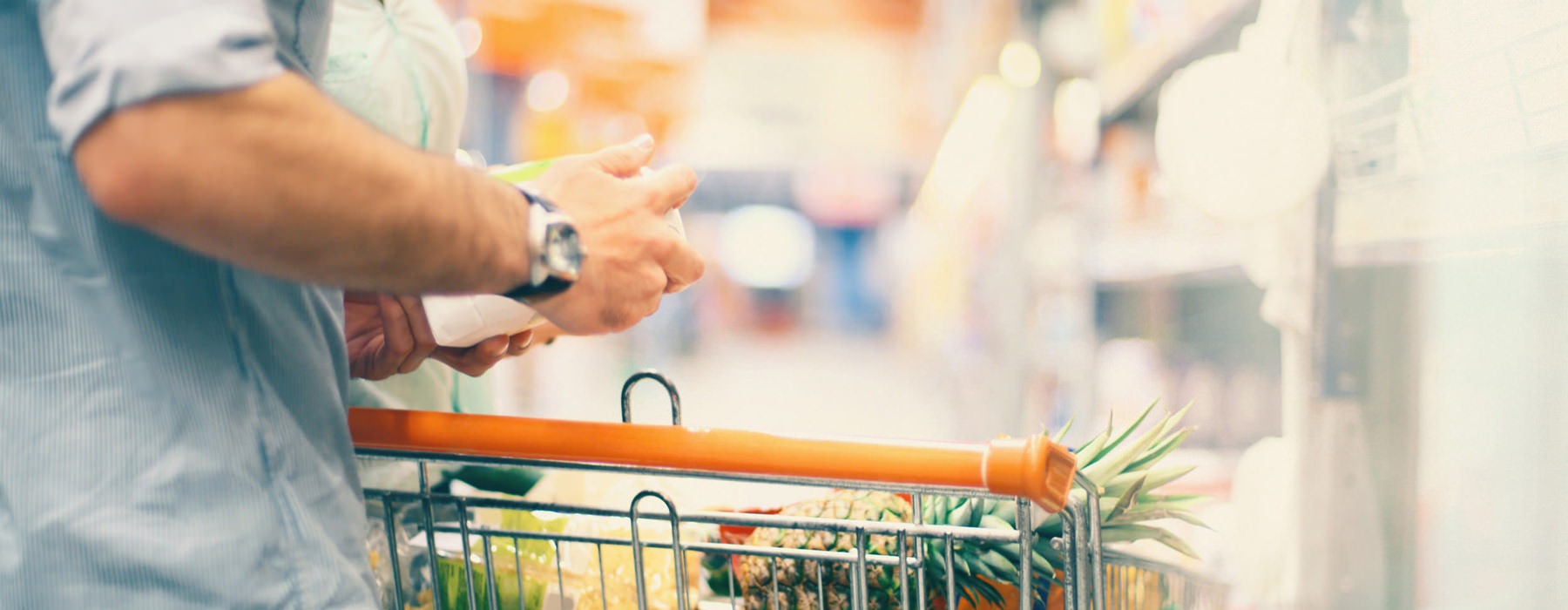 close up of man looking at a product by his shopping cart in grocery store